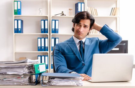 Foto de El joven guapo empleado ocupado sentado en la oficina - Imagen libre de derechos
