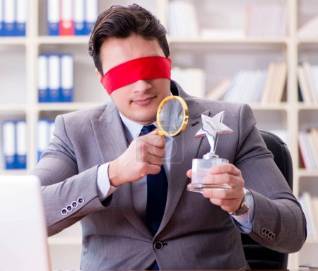 Foto de El hombre de negocios con los ojos vendados sentado en el escritorio en la oficina - Imagen libre de derechos