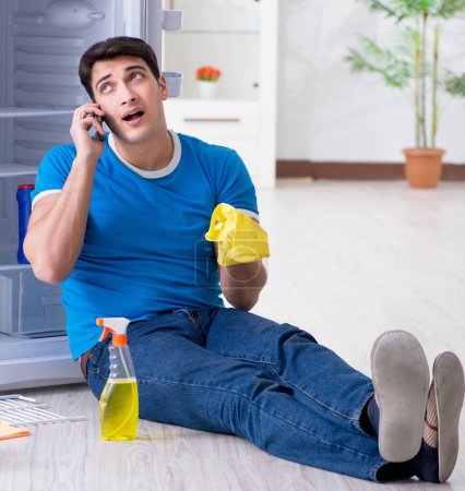 Téléchargez les photos : L'homme de nettoyage réfrigérateur dans le concept d'hygiène - en image libre de droit