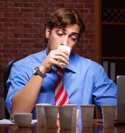Téléchargez les photos : Le jeune employé boit du café pendant son quart de nuit - en image libre de droit