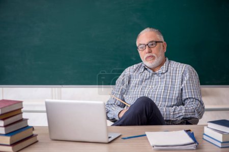 Photo for Old teacher sitting in front of green board - Royalty Free Image