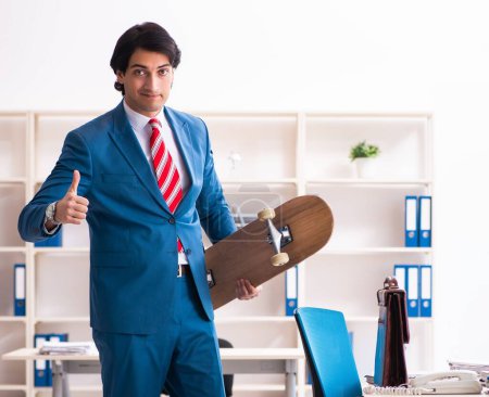 Téléchargez les photos : Le jeune homme d'affaires beau avec longboard dans le bureau - en image libre de droit
