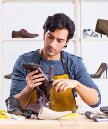 Téléchargez les photos : Le jeune homme réparant des chaussures en atelier - en image libre de droit
