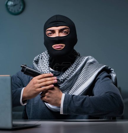 Téléchargez les photos : Le terroriste cambrioleur avec arme à feu travaillant à l'ordinateur - en image libre de droit