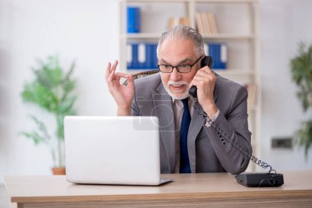 Téléchargez les photos : Ancien employé parlant par téléphone sur le lieu de travail - en image libre de droit