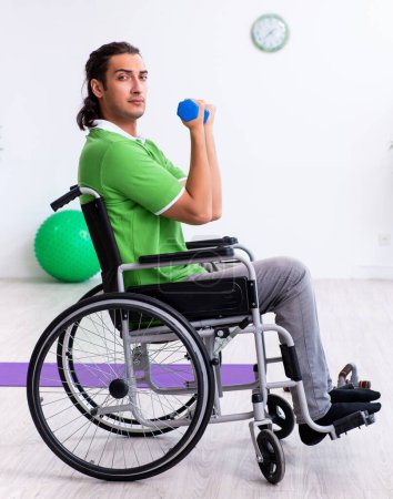 Photo for The young man in wheel-chair doing exercises indoors - Royalty Free Image
