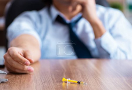 Téléchargez les photos : Le jeune homme ayant des problèmes avec les narcotiques sur le lieu de travail - en image libre de droit
