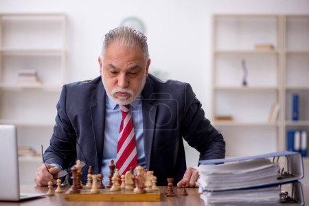Foto de Viejo empleado jugando ajedrez en el lugar de trabajo - Imagen libre de derechos