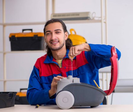 Téléchargez les photos : Le jeune entrepreneur réparation aspirateur à l'atelier - en image libre de droit