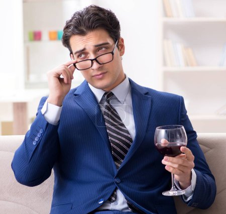 Téléchargez les photos : L'homme d'affaires buvant du vin assis à la maison - en image libre de droit