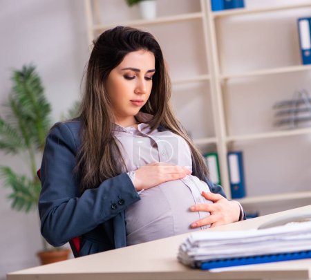 Foto de La joven embarazada que trabaja en la oficina - Imagen libre de derechos