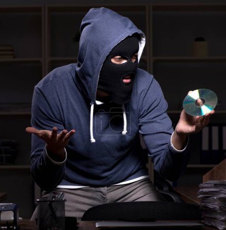Téléchargez les photos : Le voleur mâle dans la cagoule dans le bureau la nuit - en image libre de droit