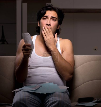 Téléchargez les photos : Le jeune homme calcule les dépenses nuit à la maison - en image libre de droit
