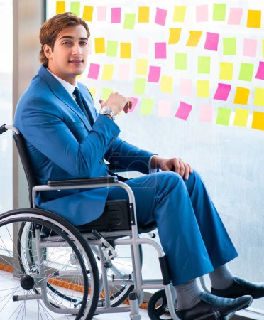 Téléchargez les photos : Jeune homme beau en fauteuil roulant avec de nombreuses priorités contradictoires - en image libre de droit