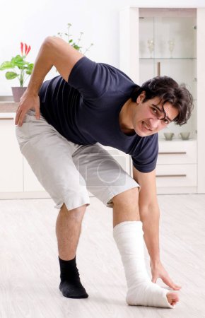 Téléchargez les photos : La jambe blessée jeune homme souffrant à la maison - en image libre de droit