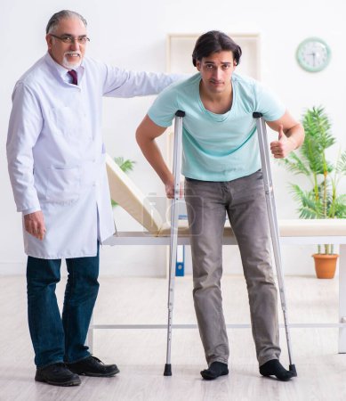 Téléchargez les photos : La jeune jambe blessé homme patient visite vieux médecin - en image libre de droit