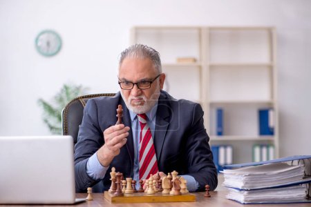 Foto de Viejo empleado jugando ajedrez en el lugar de trabajo - Imagen libre de derechos