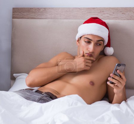 Téléchargez les photos : L'homme sexy dans le lit portant un chapeau de Père Noël dans le concept de Noël - en image libre de droit