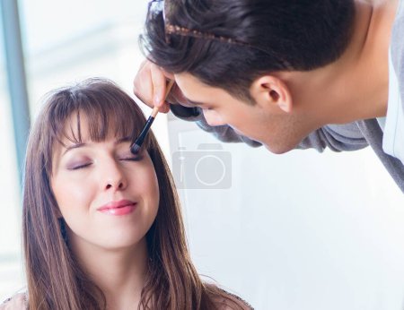 Téléchargez les photos : L'homme faisant maquillage pour femme mignonne dans le salon de beauté - en image libre de droit