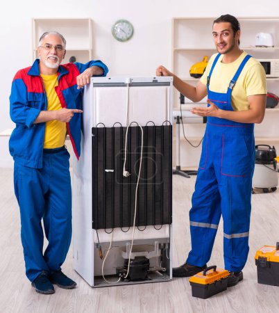 Téléchargez les photos : Les deux entrepreneurs réparent le réfrigérateur à l'atelier - en image libre de droit