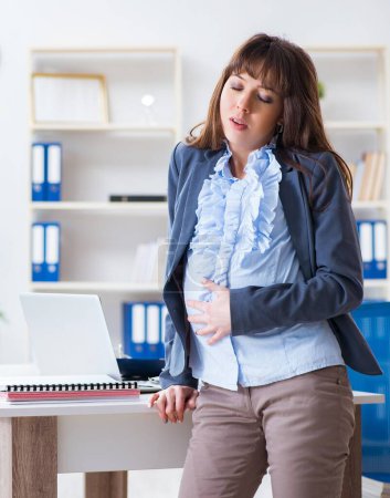 Foto de La mujer embarazada luchando para hacer el trabajo en la oficina - Imagen libre de derechos