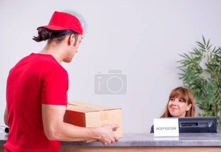 Photo for The young male courier delivering box to hotels reception - Royalty Free Image