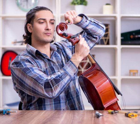 Photo for The young handsome repairman repairing cello - Royalty Free Image
