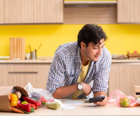 Foto de El joven calculando los gastos de verduras en la cocina - Imagen libre de derechos