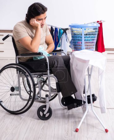 Téléchargez les photos : Le jeune homme en fauteuil roulant fait du repassage à la maison - en image libre de droit