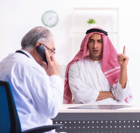 Téléchargez les photos : Le jeune homme arabe visitant médecin masculin expérimenté - en image libre de droit