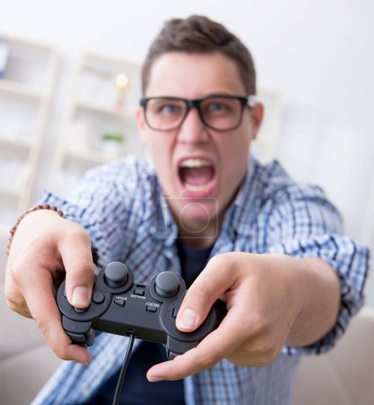 Téléchargez les photos : Le jeune homme jouant à des jeux informatiques à la maison - en image libre de droit