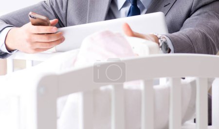 Téléchargez les photos : Jeune homme d'affaires essayant de travailler de la maison de soins après le nouveau-né - en image libre de droit