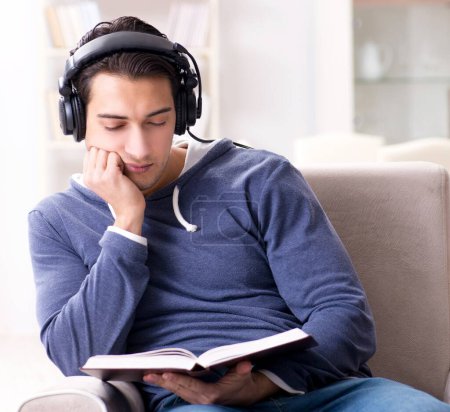 Téléchargez les photos : Le jeune homme lisant le livre et écoutant le livre audio - en image libre de droit