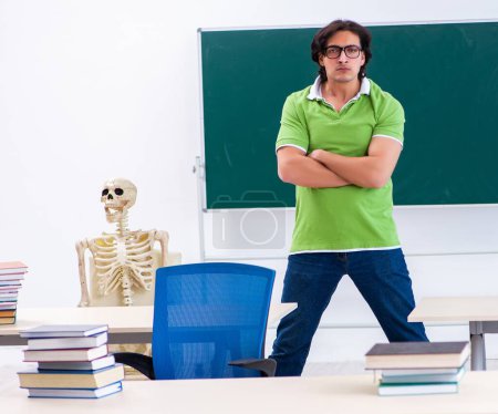 Téléchargez les photos : L'étudiant masculin drôle dans la salle de classe avec squelette - en image libre de droit