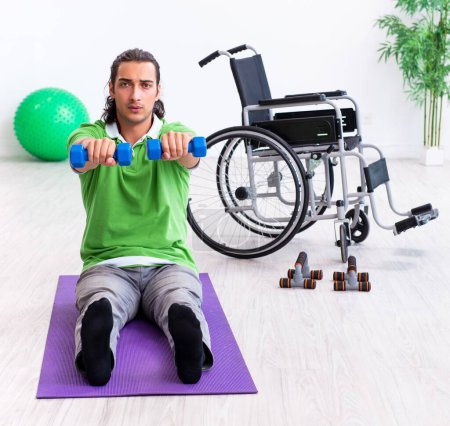 Téléchargez les photos : Le jeune homme en fauteuil roulant faisant des exercices à l'intérieur - en image libre de droit