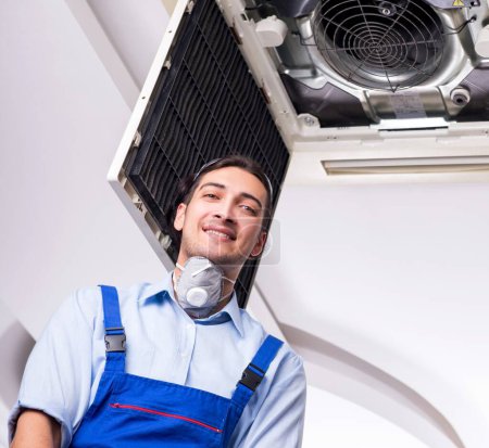Foto de El joven reparador reparando la unidad de aire acondicionado del techo - Imagen libre de derechos