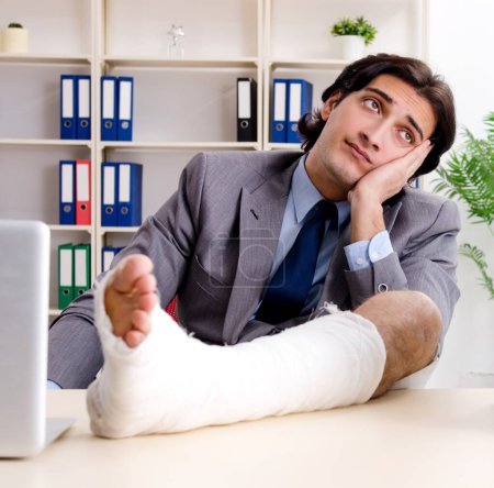 Foto de El empleado lesionado pierna que trabaja en la oficina - Imagen libre de derechos
