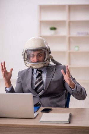 Téléchargez les photos : Young businessman employee wearing spacesuit at workplace - en image libre de droit