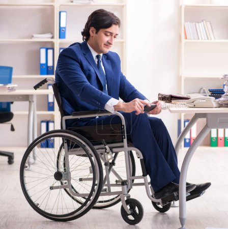 Foto de El joven empleado en silla de ruedas que trabaja en la oficina - Imagen libre de derechos
