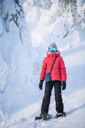 Téléchargez les photos : Mignon pré-adolescent fille randonnée en raquettes dans la forêt d'hiver parmi les arbres recouverts de neige en Laponie Finlande - en image libre de droit