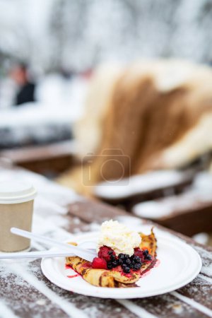 Foto de Deliciosas crepas con bayas y crema batida servida al aire libre en el día de invierno nevado - Imagen libre de derechos