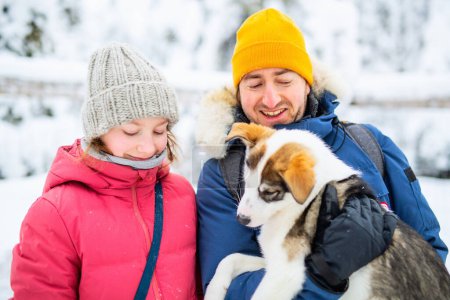 Foto de Familia del padre y su adorable hija preadolescente abrazándose con un cachorro husky al aire libre en el día de invierno en Laponia Finlandia - Imagen libre de derechos
