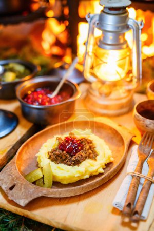 Foto de Reno salteado de comida finlandesa tradicional con puré de papas y arándanos rojos servidos en cabaña de lappish al lado de fuego abierto - Imagen libre de derechos