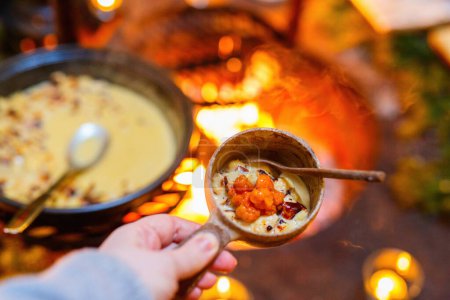 Foto de Delicioso queso horneado lapón con mermelada de mora turbia servido en un tazón de madera en una cabaña de lapislázuli junto a un fuego abierto - Imagen libre de derechos