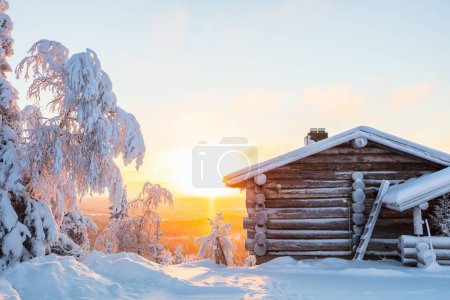 Téléchargez les photos : Beau paysage hivernal avec cabane en bois et arbres enneigés au coucher du soleil en Laponie Finlande - en image libre de droit