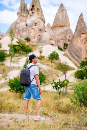 Photo for Young man exploring valley with rock formations and fairy chimneys near Uchisar castle in Cappadocia Turkey - Royalty Free Image