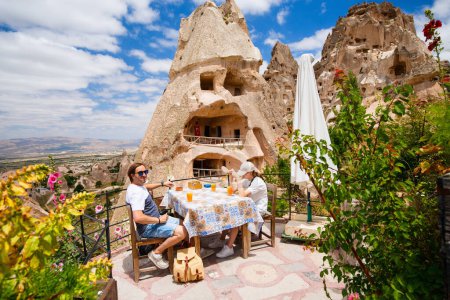Foto de Familia de padre e hija adolescente descansando en un pequeño café mientras exploran Capadocia en Turquía disfrutando de la vista de formaciones rocosas y chimeneas de hadas cerca del castillo de Uchisar - Imagen libre de derechos