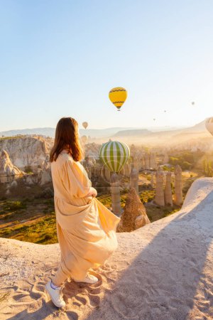Foto de Young woman admire scenery of hot air balloons flying over Love valley with rock formations and fairy chimneys in Cappadocia Turkey - Imagen libre de derechos
