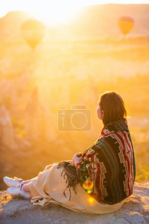 Téléchargez les photos : Young woman admire scenery of hot air balloons flying over Love valley with rock formations and fairy chimneys in Cappadocia Turkey - en image libre de droit