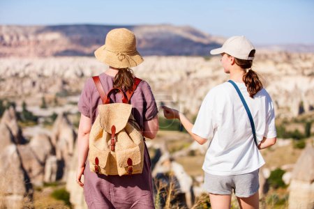 Photo for Back view of mother and daughter family enjoying view of valley with rock formations and fairy chimneys in Cappadocia Turkey - Royalty Free Image